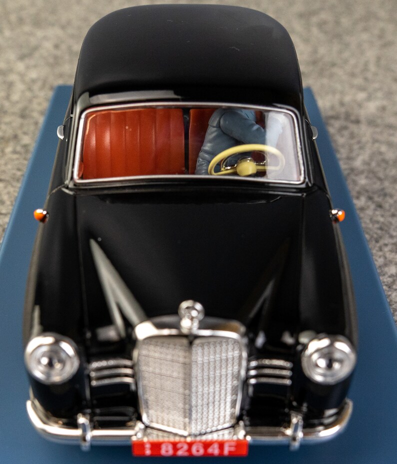 Puede incluir: Modelo de coche negro vintage con interior rojo. El coche tiene una parrilla cromada, faros y una placa de matr&iacute;cula que dice "8264F". El volante es amarillo. El modelo est&aacute; sobre una superficie azul.