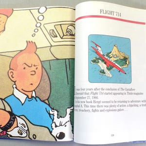 Puede incluir: Libro abierto con una ilustraci&oacute;n de c&oacute;mic de Tint&iacute;n y Mil&uacute;, y una p&aacute;gina con un dibujo de un avi&oacute;n rojo y blanco. El texto "FLIGHT 714" est&aacute; en la parte superior de la p&aacute;gina derecha.