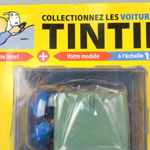 Pu&ograve; includere: Un oggetto da collezione di Tintin confezionato con un modello di veicolo verde in scala 1/24. La confezione &egrave; gialla con testo francese, tra cui "COLLECTIONNEZ LES VOITURES DE TINTIN". Include un'illustrazione di Tintin e Mil&ugrave;.