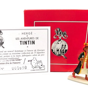 Pode incluir: Uma pequena figura de metal detalhada de um personagem da série de banda desenhada do Tintin, "As Aventuras de Tintin". A figura é pintada em cores brilhantes, incluindo vermelho, amarelo, preto e branco. A personagem usa um turbante e segura um pincel e um balde. A figura é exibida numa base branca. A caixa é vermelha com um rótulo branco que diz "Hergé - As Aventuras de Tintin - Pixi - 001690".