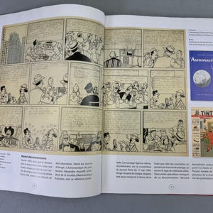 Puede incluir: Un libro abierto con una tira c&oacute;mica en blanco y negro con m&uacute;ltiples paneles. El c&oacute;mic muestra escenas de personas en varios entornos. Tambi&eacute;n se ven dos portadas de libros, una con la palabra "Astronautique" y una ilustraci&oacute;n de la luna, y otra con "Tint&iacute;n".