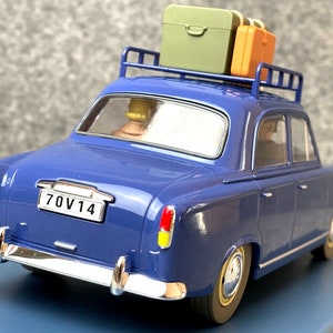 May include: A blue vintage car model with a luggage rack holding two suitcases. The car has a license plate that reads "70V14". The car's body is a deep blue, with chrome accents and yellow and red taillights.
