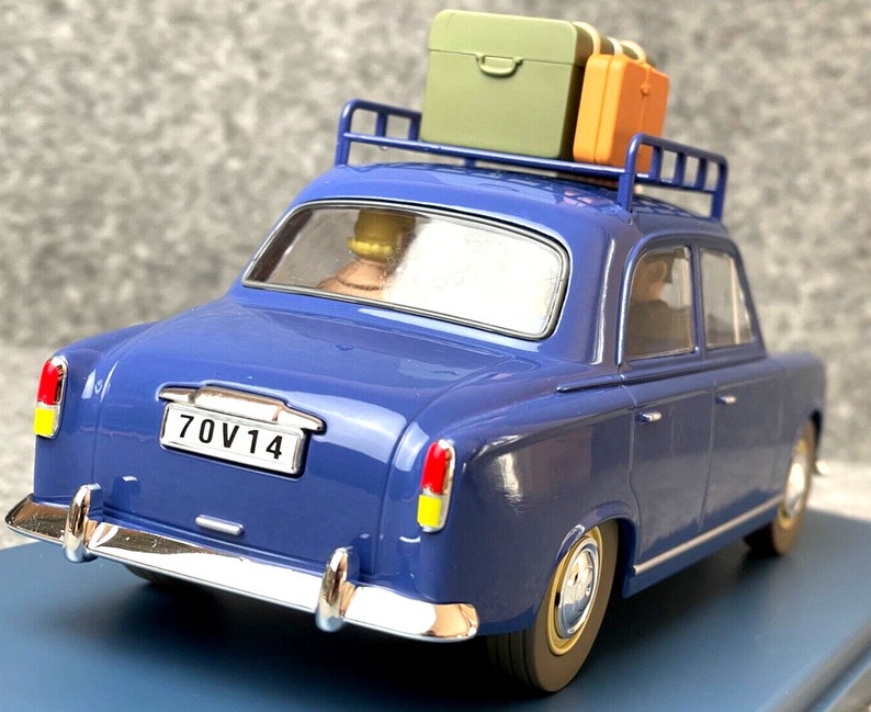 May include: A blue vintage car model with a luggage rack holding two suitcases. The car has a license plate that reads "70V14". The car's body is a deep blue, with chrome accents and yellow and red taillights.