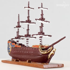 Könnte beinhalten: Ein detailliertes Modell eines braunen Segelschiffs mit weißen Akzenten an den Segeln. Das Schiff hat einen goldenen Besatz und ist auf einem Holzsockel montiert.