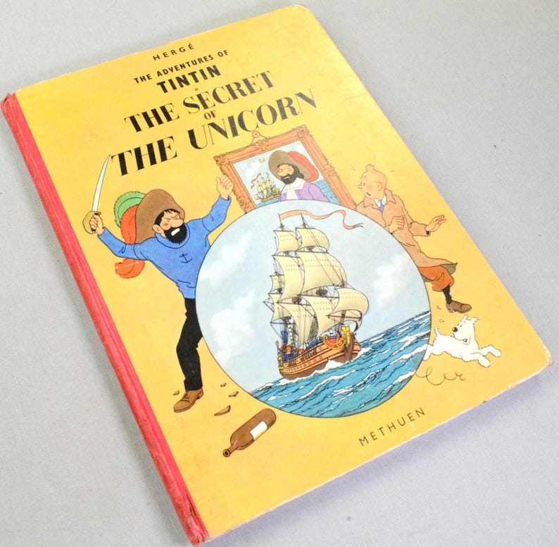 May include: A vintage copy of "The Adventures of Tintin: The Secret of the Unicorn" by Herg&eacute;. The cover is yellow with red edges and features illustrations of Captain Haddock, a ship, and other characters. The book is published by Methuen.