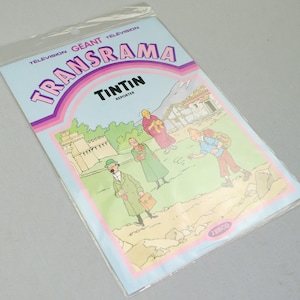 Puede incluir: Un c&oacute;mic vintage "Transrama" con Tint&iacute;n, el reportero. La portada tiene un fondo azul claro con el t&iacute;tulo en rosa y morado. La ilustraci&oacute;n muestra personajes en un paisaje monta&ntilde;oso.