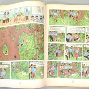 May include: An open book featuring comic panels with illustrations. The panels depict characters in blue shirts and red pants, exploring a jungle setting with a white dog. The artwork is in a classic comic book style, with speech bubbles.