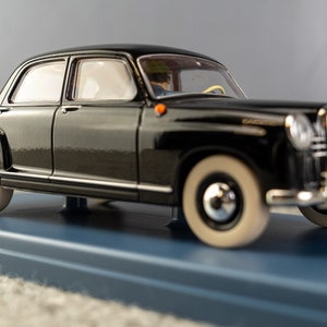 Puede incluir: Un modelo de coche negro vintage con neum&aacute;ticos de banda blanca y detalles cromados. El coche est&aacute; sobre una base azul. El modelo tiene una parrilla delantera detallada y una matr&iacute;cula roja. La carrocer&iacute;a del coche es brillante.