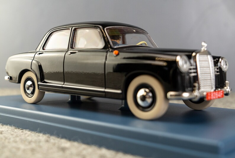 Puede incluir: Un modelo de coche negro vintage con neum&aacute;ticos de banda blanca y detalles cromados. El coche est&aacute; sobre una base azul. El modelo tiene una parrilla delantera detallada y una matr&iacute;cula roja. La carrocer&iacute;a del coche es brillante.