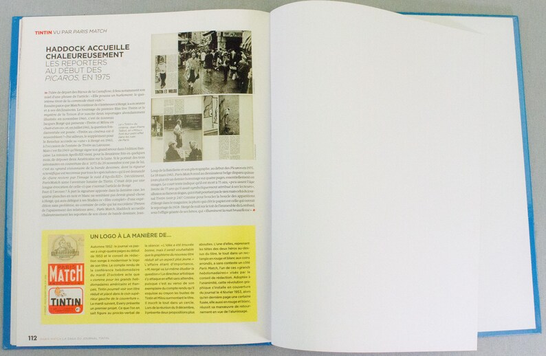 May include: An open book with a blue cover, featuring text and images. The left page has text and black and white photos, with a yellow box containing text and logos. The right page is blank. The text includes "HADDOCK ACCUEILLE CHALEUREUSEMENT LES REPORTERS AU DEBUT DES PICAROS EN 1975".