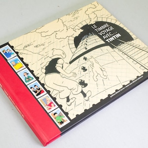 May include: A hardcover book featuring a black and white illustration of a cartoon character running near a tunnel. The book has a red spine with text and a series of postage stamp-like images. The title "LE TIMBRE VOYAGE AVEC... TINTIN" is displayed on the cover.