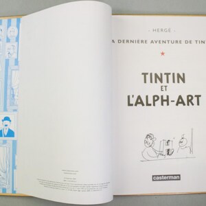 Może przedstawiać: Otwarta książka z tytułem "Tintin et l'Alph-Art" w czarnym tekście. Strony książki są białe, z ilustracjami i tekstem. Lewa strona ma niebiesko-białe oprawione portrety. Książka to komiks.