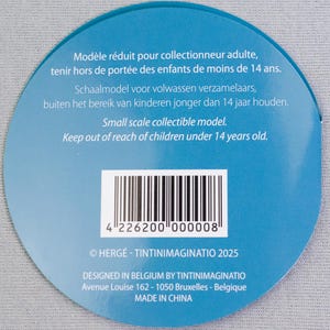 以下が含まれることがあります： 複数の言語でテキストが書かれた、丸い水色のラベル。「Small scale collectible model」の文字が含まれています。バーコードと「14歳未満のお子様の手の届かないところに保管してください」というテキストも含まれています。