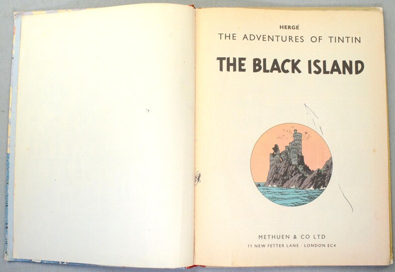 K&ouml;nnte beinhalten: Aufgeschlagenes Buch mit dem Titel "Die Schwarze Insel" von Herg&eacute;. Das Cover zeigt eine runde Illustration einer felsigen Insel mit Burg und Meer. Der Verlag des Buches ist Methuen & Co Ltd.