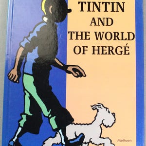 Puede incluir: Portada del libro con Tint&iacute;n y Mil&uacute; caminando. El t&iacute;tulo es "Tint&iacute;n y el Mundo de Herg&eacute;" de Beno&icirc;t Peeters. El fondo est&aacute; dividido entre azul y beige. Publicado por Methuen.