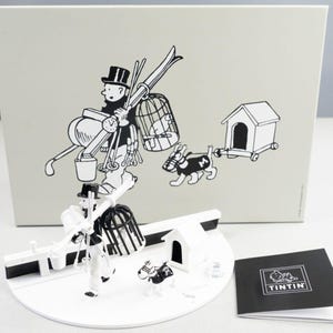 Könnte beinhalten: Ein weiß-schwarzes Figurenset mit einer Figur aus der Tintin-Comicserie. Die Figur trägt einen Vogelkäfig, Skier und andere Gegenstände. Das Set enthält auch einen Hund und eine Hundehütte. Das Figurenset steht auf einem weißen Sockel mit schwarzem Rand. Das Set wird von einem schwarz-weißen Booklet mit dem Wort "Tintin" auf dem Cover begleitet.