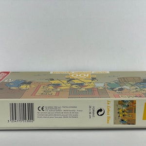 Peut inclure: Bo&icirc;te de puzzle de 100 pi&egrave;ces illustrant des personnages de la bande dessin&eacute;e "Le Lotus Bleu" d'Herg&eacute;. La bo&icirc;te est blanche avec des accents jaunes et le texte "Le Lotus Bleu" et "100" imprim&eacute; dessus. Le puzzle est fabriqu&eacute; en France.