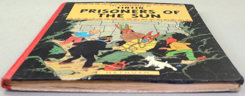 Op de afbeelding: Een vintage hardcover boek getiteld "De avonturen van Kuifje: De Zonnetempel". De omslag toont een kleurrijke illustratie van personages in een actiesc&egrave;ne. Het boek heeft een zwarte kaft met een gele titelbanner en een rode rug.