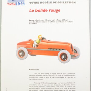 Pu&ograve; includere: Un'auto giocattolo arancione con ruote bianche, con un conducente e una statuina di cane. L'auto &egrave; un modello di "Le bolide rouge" della serie Tintin. L'immagine include testo in francese.