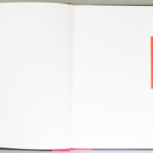May include: An open book with white pages and red accents. The right page features a red square with white text that reads "LE TIMBRE VOYAGE AVEC... TINTIN". The left page has a list of text in a smaller font.