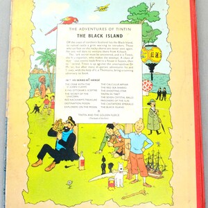 K&ouml;nnte beinhalten: Die R&uuml;ckseite eines Vintage-Tintin-Comics, "Die Abenteuer von Tim und Struppi: Die schwarze Insel". Das Cover zeigt Illustrationen von Charakteren und Szenen aus der Geschichte, mit Text, der die Handlung und andere Titel der Serie beschreibt.