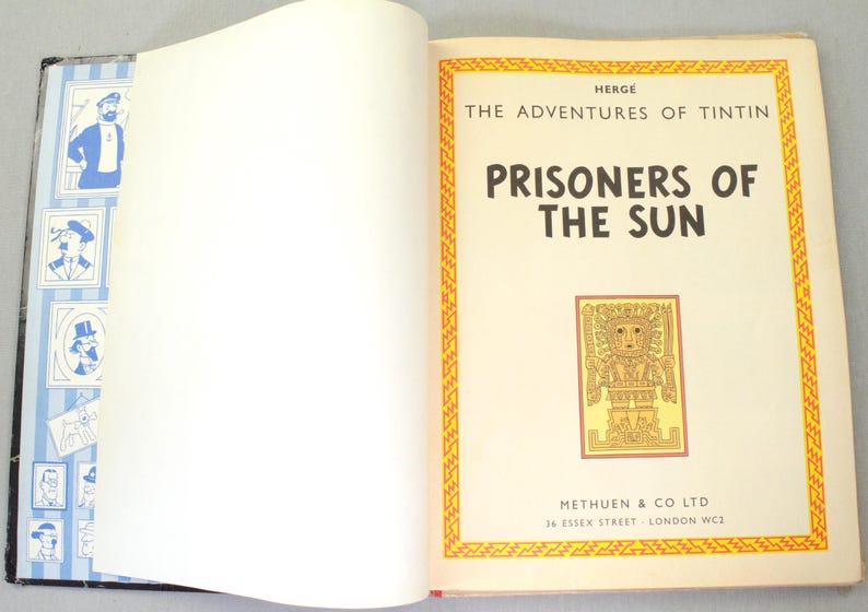 Op de afbeelding: Open boek met de titel "Prisoners of the Sun" uit de serie "De avonturen van Kuifje". De kaft heeft een gele en oranje rand met een illustratie. Uitgegeven door Methuen & Co Ltd.