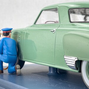 Pu&ograve; includere: Modello di auto d'epoca verde con pneumatici a fascia bianca. Due figure in miniatura in uniforme blu sembrano lavorare sull'auto. L'auto ha dettagli cromati e interni dettagliati, su una base blu.