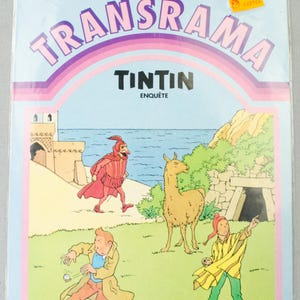 K&ouml;nnte beinhalten: Versiegelte Verpackung mit einem Comic-Cover mit dem Titel "TRANSRAMA" in gro&szlig;en, lila Buchstaben. Das Cover-Artwork zeigt Charaktere aus der "Tim und Struppi"-Serie, darunter Tim selbst, ein Lama und andere Figuren in einer farbenfrohen Au&szlig;enszene.