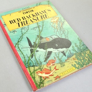 May include: A vintage copy of "Red Rackham's Treasure" by Herg&eacute;. The cover features an underwater scene with a shark-shaped submarine, fish, and seaweed. The title is in large yellow letters against a blue background.