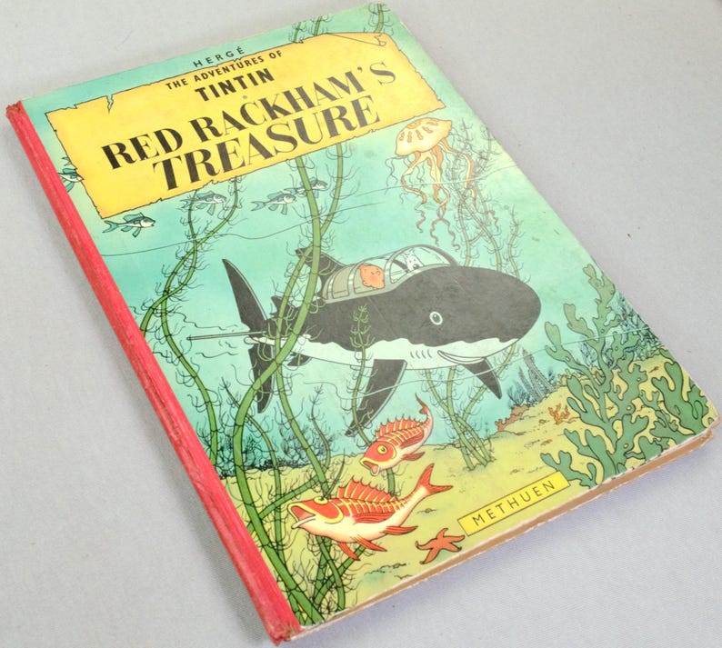 May include: A vintage copy of "Red Rackham's Treasure" by Herg&eacute;. The cover features an underwater scene with a shark-shaped submarine, fish, and seaweed. The title is in large yellow letters against a blue background.