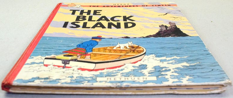 K&ouml;nnte beinhalten: Ein Vintage-Exemplar von "Die Schwarze Insel" von Herg&eacute;, aus der Reihe "Tim und Struppi". Das Cover zeigt ein Boot mit einer Figur und einem Hund auf dem Wasser, mit einer Burg auf einer Insel im Hintergrund. Das Buch hat einen roten R&uuml;cken und den Namen des Verlags.