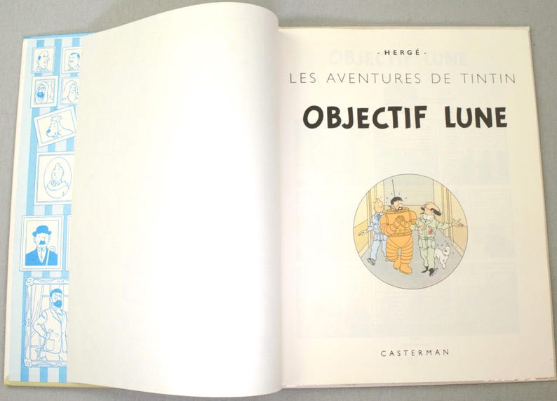 K&ouml;nnte beinhalten: Aufgeschlagenes Buch mit dem Titel "OBJECTIF LUNE" in gro&szlig;en schwarzen Buchstaben. Das Buch zeigt eine Comic-Illustration von drei Figuren in einem Kreis. Der Einband hat blau-wei&szlig; gestreifte R&auml;nder mit gerahmten Illustrationen.