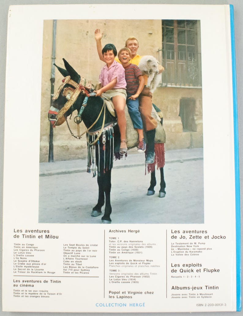 Puede incluir: Portada de libro con una fotograf&iacute;a de cuatro ni&ntilde;os montados en un burro decorado, sonriendo y saludando. El t&iacute;tulo y el autor del libro est&aacute;n en franc&eacute;s, con un fondo azul y blanco. El libro forma parte de la serie "Collection Herg&eacute;".