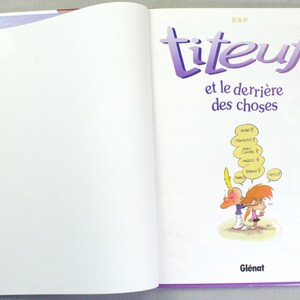 K&ouml;nnte beinhalten: Ein gebundenes Comicbuch mit dem Titel Titeuf et le derri&egrave;re des choses, Band 5. Die wei&szlig;e Titelseite zeigt violetten Text und eine kleine Comic-Illustration von zwei Figuren mit gelben Sprechblasen, die verschiedene Namen enthalten.