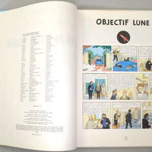 K&ouml;nnte beinhalten: Aufgeschlagenes Buch mit blau-wei&szlig;em Einband, das Cartoon-Illustrationen zeigt. Die rechte Seite zeigt Comic-Panels mit dem Titel "OBJECTIF LUNE" und einem Raketenlogo. Die Buchseiten sind wei&szlig;, die Comic-Panels farbig.