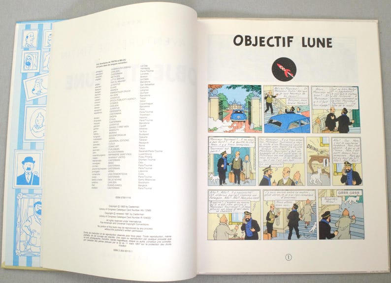 K&ouml;nnte beinhalten: Aufgeschlagenes Buch mit blau-wei&szlig;em Einband, das Cartoon-Illustrationen zeigt. Die rechte Seite zeigt Comic-Panels mit dem Titel "OBJECTIF LUNE" und einem Raketenlogo. Die Buchseiten sind wei&szlig;, die Comic-Panels farbig.