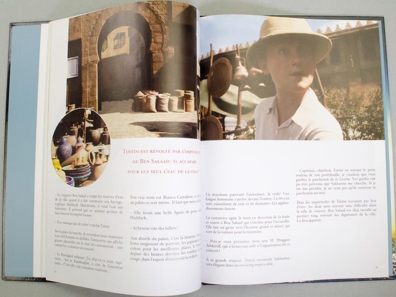 May include: A book spread with photographs and text. One image shows a person in a safari hat. Another image shows an archway and sacks. French text reads "TINTIN EST REVOLTE PAR L'IMPUDEUR DE BEN SALAAD: IL ACCAPARE POUR LUI SEUL L'EAU DE LA VILLE."