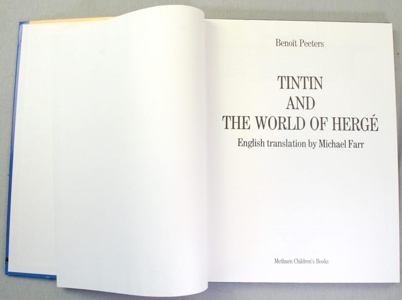 Puede incluir: Un libro abierto con el t&iacute;tulo "TINTIN AND THE WORLD OF HERG&Eacute;" en negro. El nombre del autor, Benoit Peeters, y del traductor, Michael Farr, tambi&eacute;n est&aacute;n presentes. El libro tiene una encuadernaci&oacute;n azul.