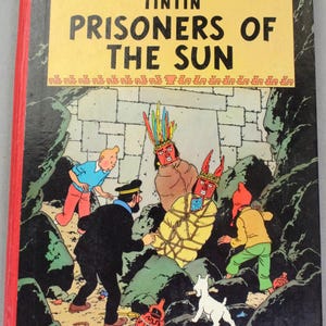 Op de afbeelding: Een vintage hardcover boek getiteld "De avonturen van Kuifje: De Zonnetempel". De omslag toont een kleurrijke illustratie van Kuifje en andere personages in een grot. Het boek heeft een rode rug en de naam van de uitgever, Methuen, is zichtbaar.