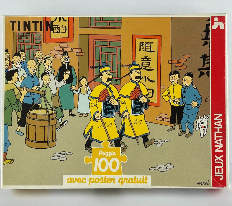 Peut inclure: Un puzzle de 100 pi&egrave;ces repr&eacute;sentant des personnages de la s&eacute;rie de bandes dessin&eacute;es Tintin. Le puzzle repr&eacute;sente une sc&egrave;ne du livre "Le Lotus Bleu" avec Tintin et son chien Milou dans un march&eacute; de rue chinois. La bo&icirc;te de puzzle comprend un poster.
