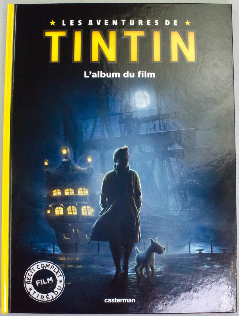 May include: A book cover with the title "LES AVENTURES DE TINTIN" in yellow. The image shows a person and a dog standing before a ship at night. The text "L'album du film" is also visible on the cover.