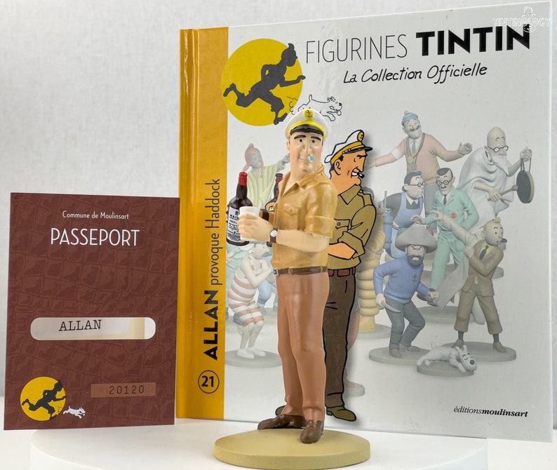 May include: A brown and tan figurine of Captain Haddock from the Tintin comic series. He is holding a bottle of alcohol and a glass. The figurine is standing on a base with the text "Allan provoque Haddock" and the number "21". The background is a book cover with the text "Figurines Tintin La Collection Officielle" and a picture of Tintin running.