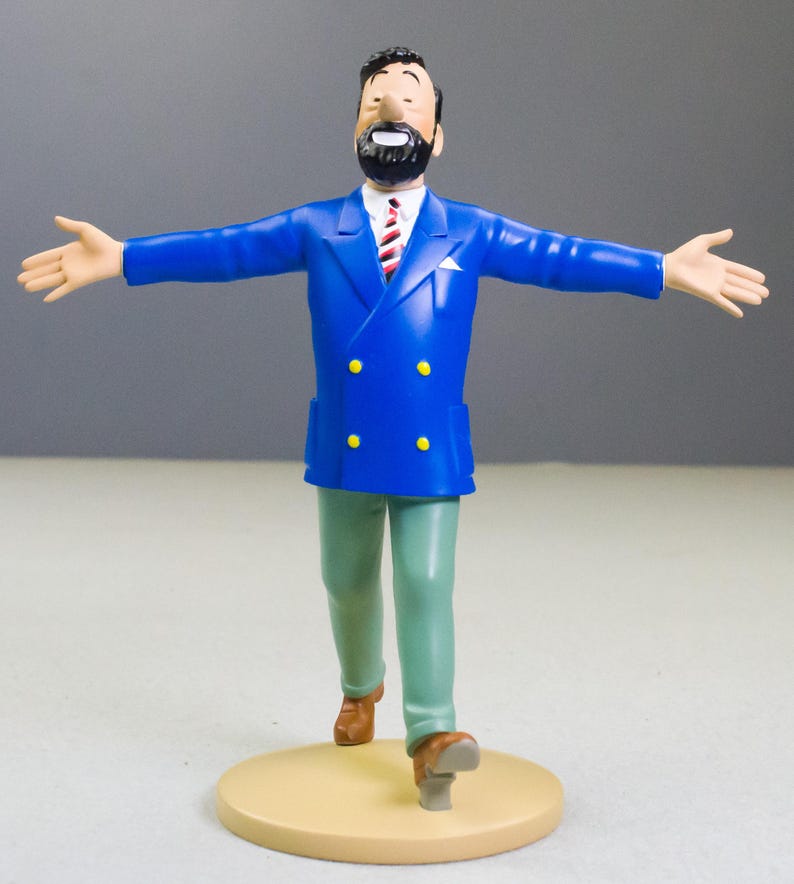 以下が含まれることがあります： 黒いひげと髪の男性のフィギュア。青いダブルブレストのジャケット、赤と白のストライプのネクタイが付いた白いシャツ、緑のズボンを着用しています。フィギュアは、腕を広げて、タン色のベースの上に立っています。