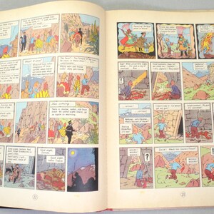 Op de afbeelding: Open boek met een dubbele pagina met kleurrijke stripverhalen. De illustraties tonen sc&egrave;nes met personages in verschillende omgevingen, waaronder buitenlandschappen en interieurs. Tekstballonnen bevatten dialogen.