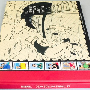 May include: A hardcover book titled "LE TIMBRE VOYAGE AVEC... TINTIN" featuring a comic illustration of Tintin falling from a tunnel. The cover has a red spine and a series of Tintin-themed stamps along the bottom edge.