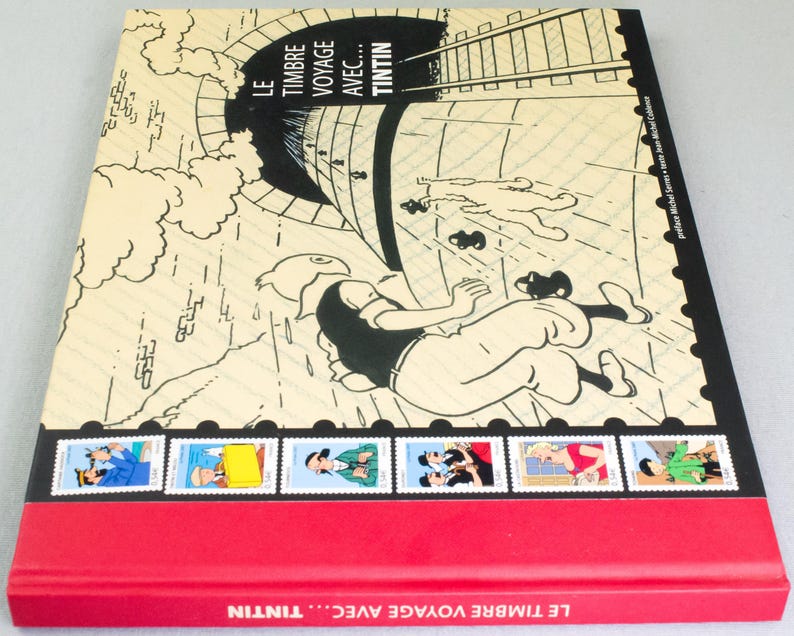 May include: A hardcover book titled "LE TIMBRE VOYAGE AVEC... TINTIN" featuring a comic illustration of Tintin falling from a tunnel. The cover has a red spine and a series of Tintin-themed stamps along the bottom edge.