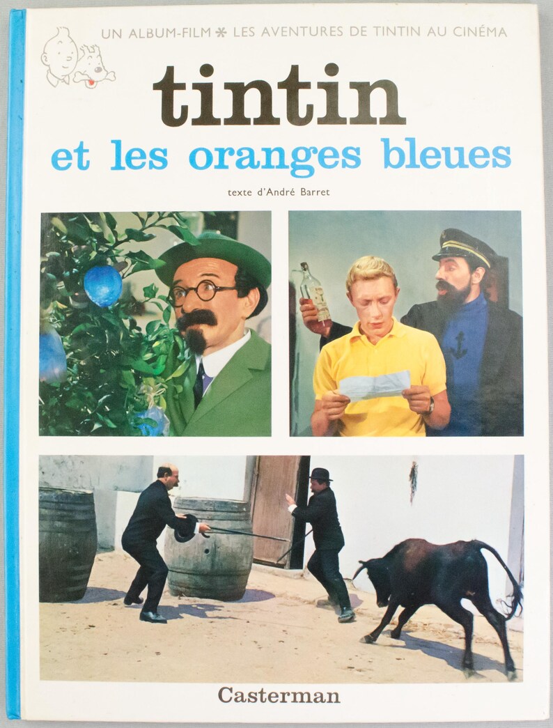 Puede incluir: Portada del libro "Tint&iacute;n y las naranjas azules". El t&iacute;tulo est&aacute; en letras negras grandes sobre un t&iacute;tulo azul. La portada presenta im&aacute;genes de personajes y escenas de la pel&iacute;cula, con el nombre del editor, Casterman, en la parte inferior.