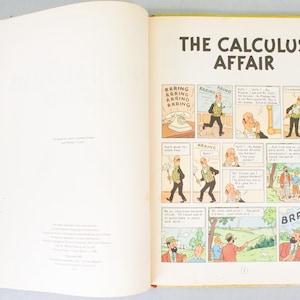 May include: Open book with a yellow cover, displaying a comic strip titled "The Calculus Affair." The comic features panels with illustrations and speech bubbles. The pages are cream-colored.