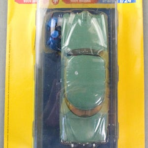Pu&ograve; includere: Modello di auto verde vintage in una custodia di plastica trasparente, parte della collezione "Tintin". La confezione &egrave; gialla con testo francese e il sito web www.voitures-tintin.com.