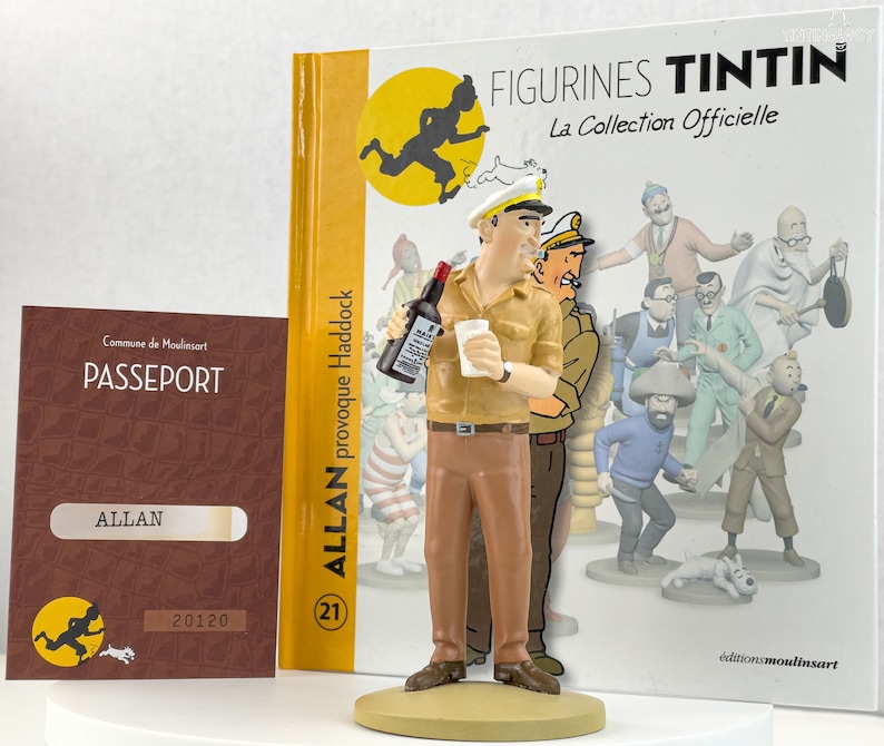May include: A figurine of Captain Haddock from the Tintin comic series. He is wearing a brown uniform with a white cap and holding a bottle of alcohol and a glass. The figurine is standing on a base with the text "Allan provoque Haddock" and "21" printed on it. The background shows a book cover with the text "Figurines Tintin La Collection Officielle" and a group of characters from the Tintin comics.